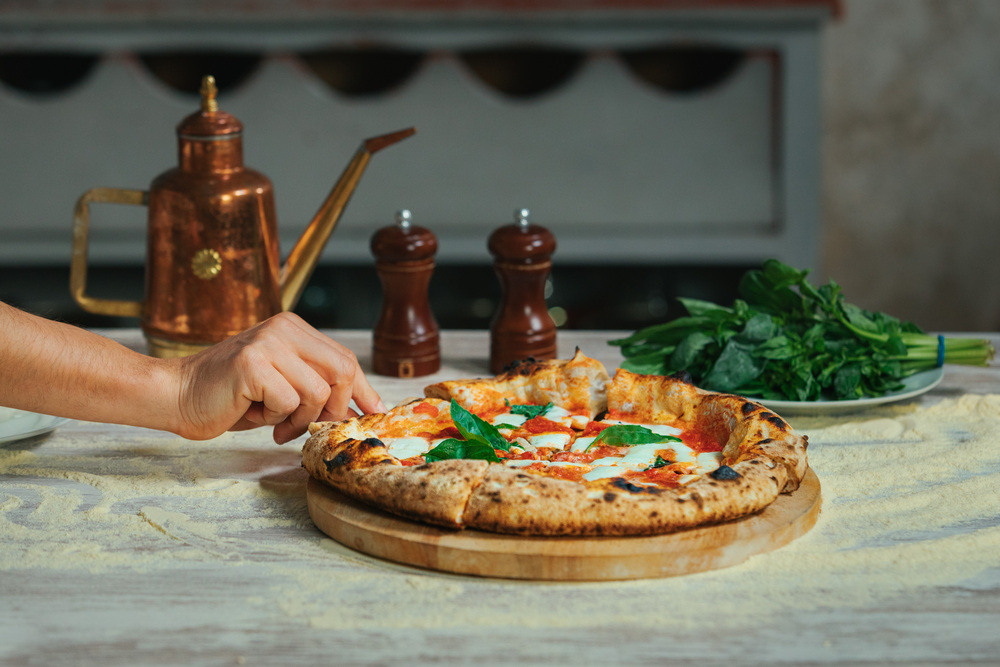 Plato de pizza de calabaza y panceta, mano cogiendo un trozo con fondo de una cocina, albahaca y utensilios de cocina, pizzas diferentes