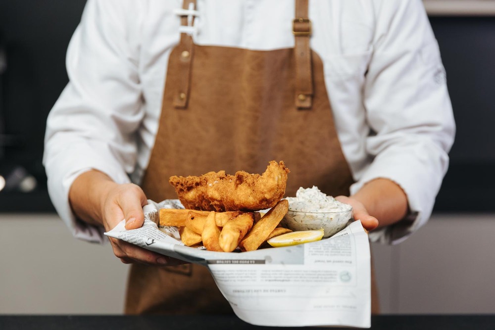 Manos con plato de fish and chips, cómo hacer salsa tártara