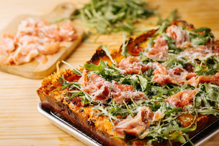 Pizza de Detroit con ingredientes al fondo, pizzas de Estados Unidos