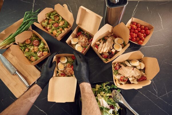 Meat, vegetables, tomatoes, eggs on the table. Man is packing food into the paper eco boxes. Indoors, restaurant